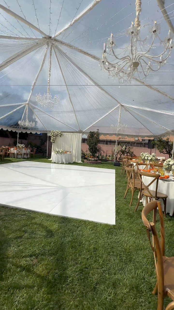 Clear dome tent wedding setup with white dance floor and crystal chandeliers on grass