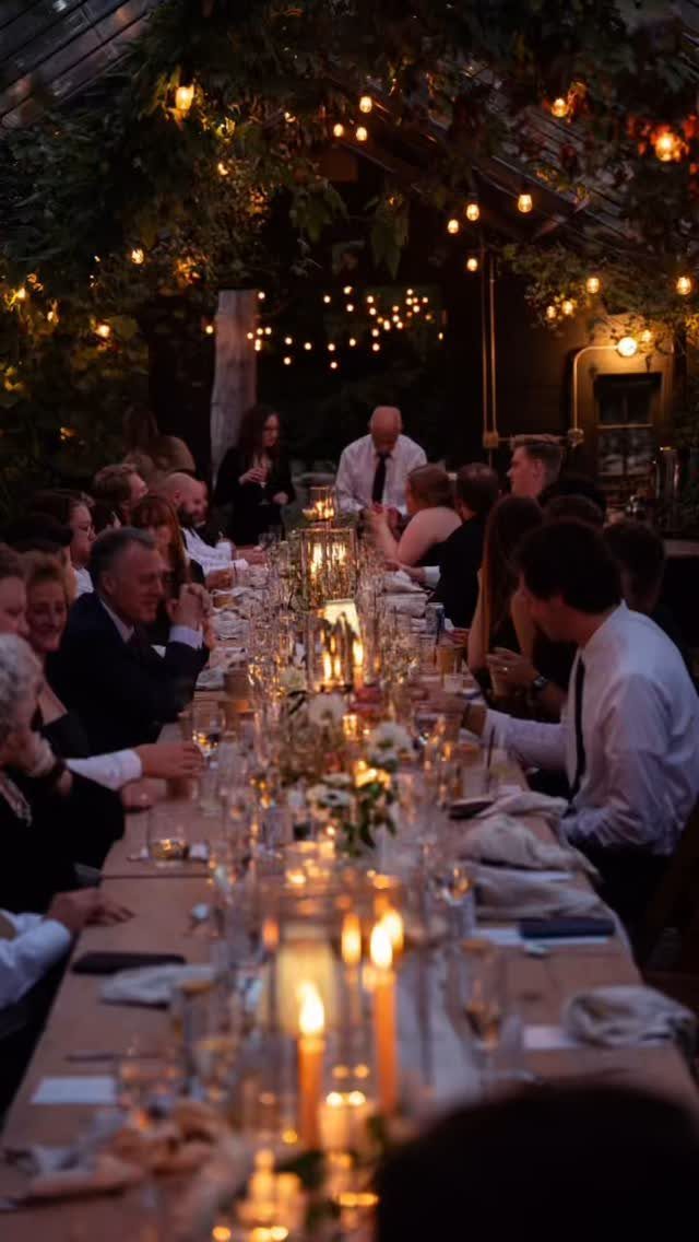 Long wedding banquet table with guests and warm candle lighting in a rustic venue