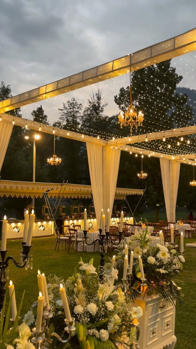 Outdoor wedding reception setup with white canopy, fairy lights, and elegant floral centerpieces.