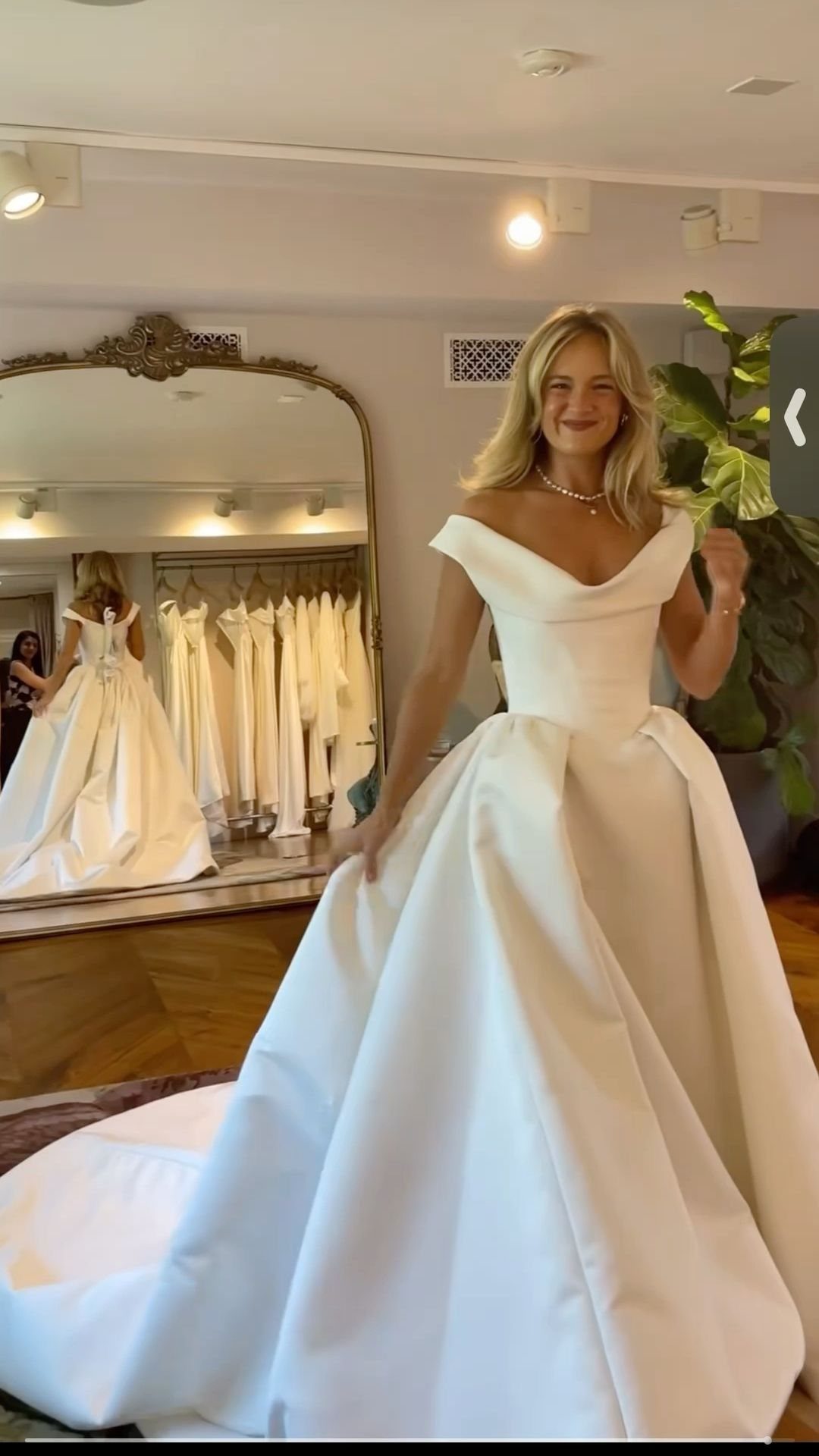 Woman wearing a white satin ball gown wedding dress in a bridal boutique.