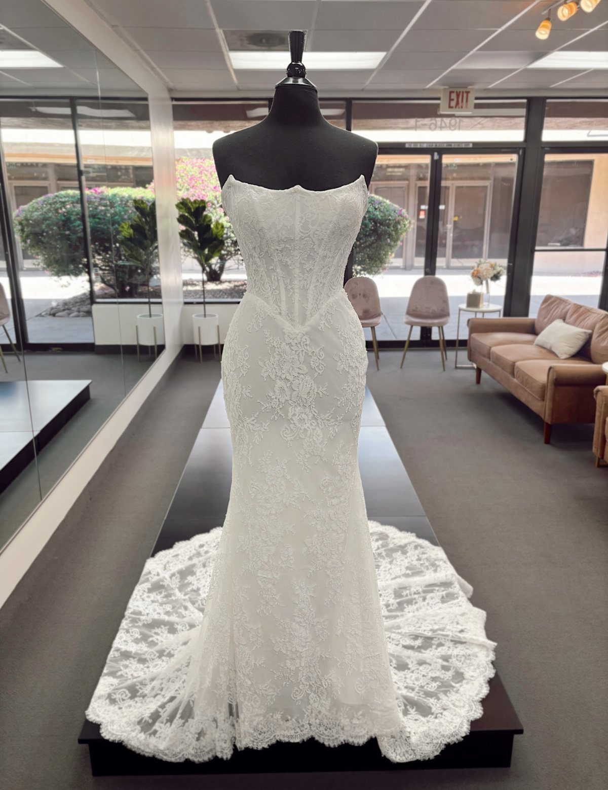 6 Basque Wedding Dress Ideas, from Lace to Ball Gowns 5 White lace wedding dress with basque waist on a black mannequin in a boutique.