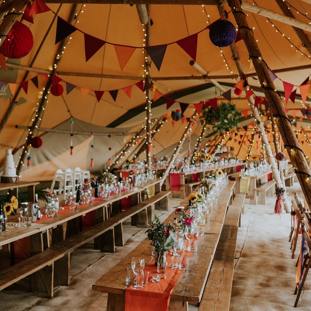 Festive tent interior with long wooden tables, orange runners, and colorful bunting flags.