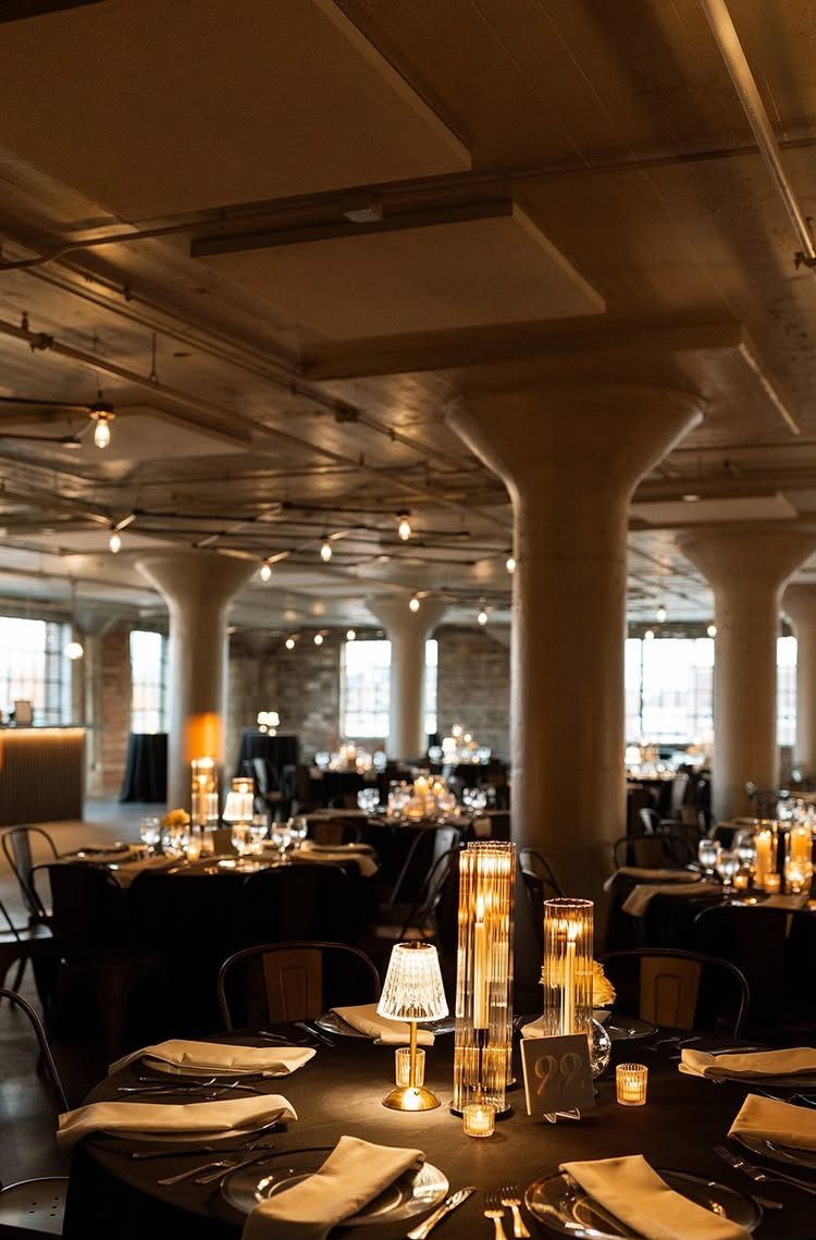 Industrial event space with concrete columns and tables set with warm glowing lamps