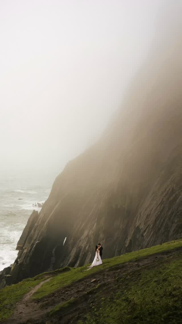 Bride and groom embracing on a foggy cliffside overlooking the ocean