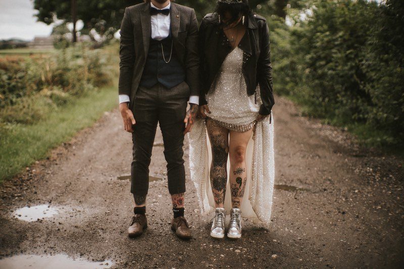Wedding couple on a dirt path, bride wearing a leather jacket and glitter boots.