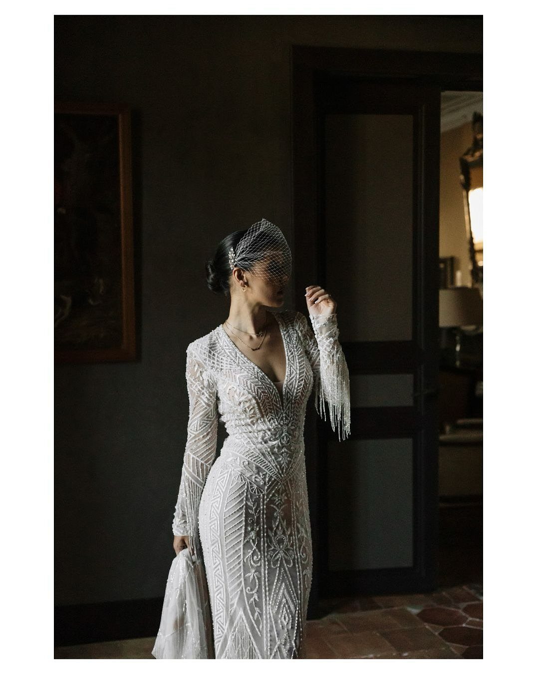 Bride in a beaded white wedding gown and birdcage veil in a moody room
