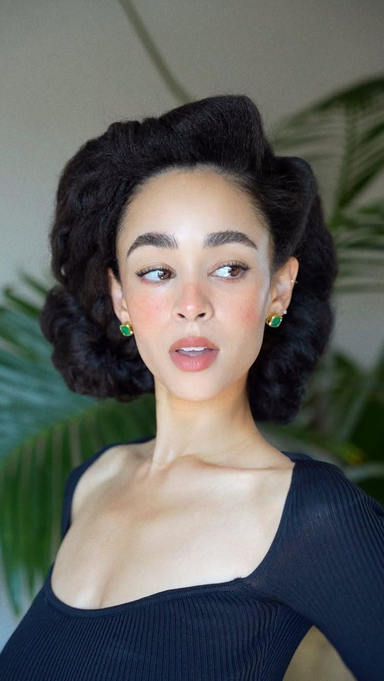 11 Black Natural Hair Wedding Hairstyles for Brides 7 Woman with a sculpted retro-inspired black hair updo and green earrings.