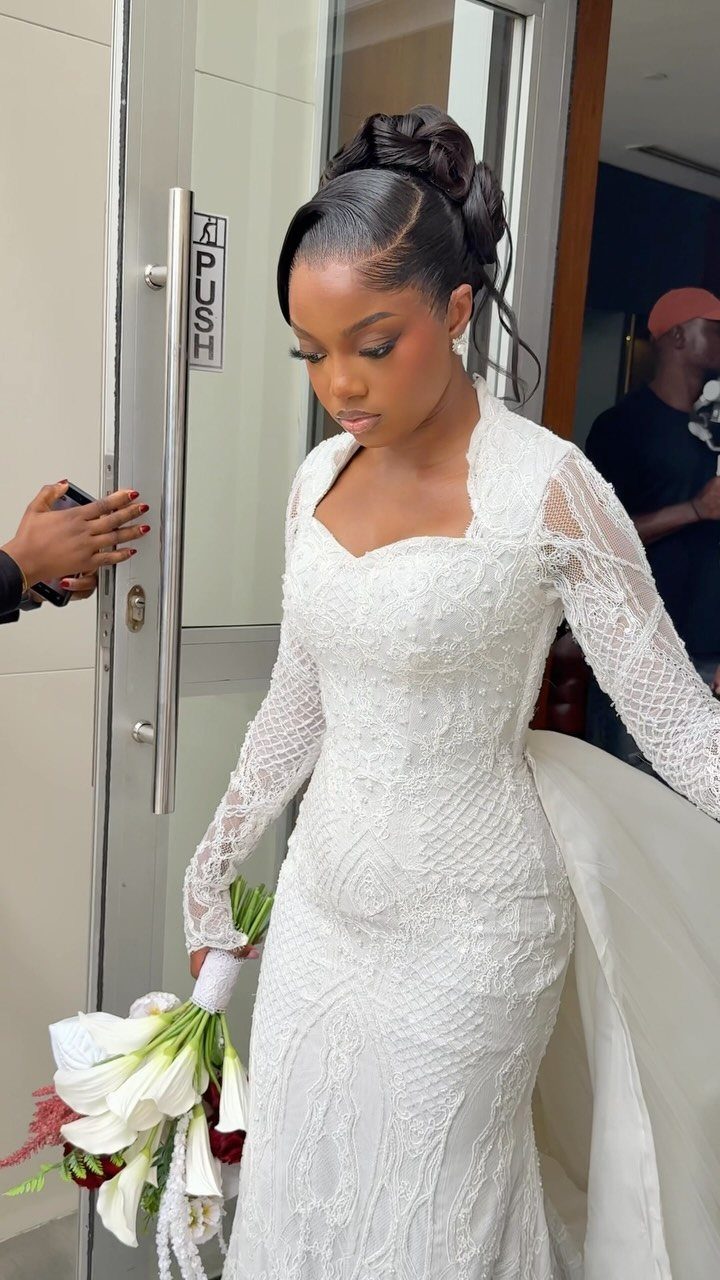11 Black Natural Hair Wedding Hairstyles for Brides 10 Woman in white lace wedding dress with a sleek high bun hairstyle and bouquet.