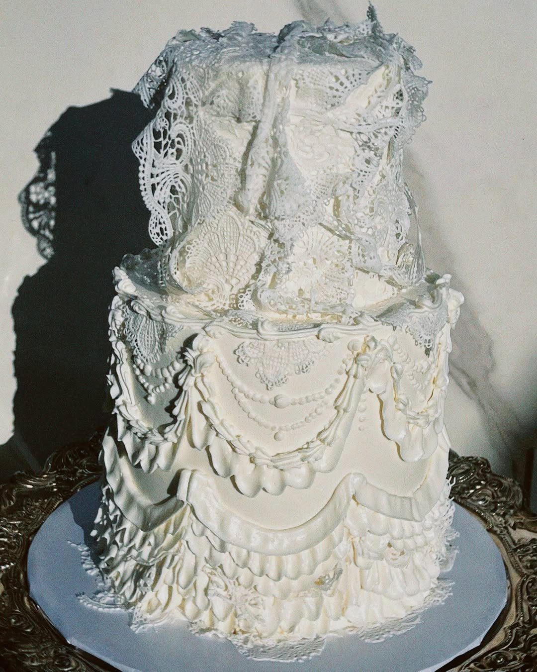 Multi-tiered white wedding cake decorated with intricate edible lace and draped frosting.