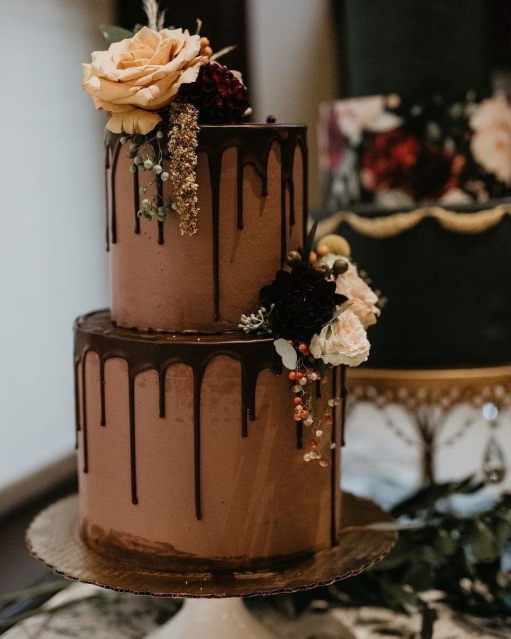 Two-tier chocolate cake with glossy chocolate drips and peach and red roses.
