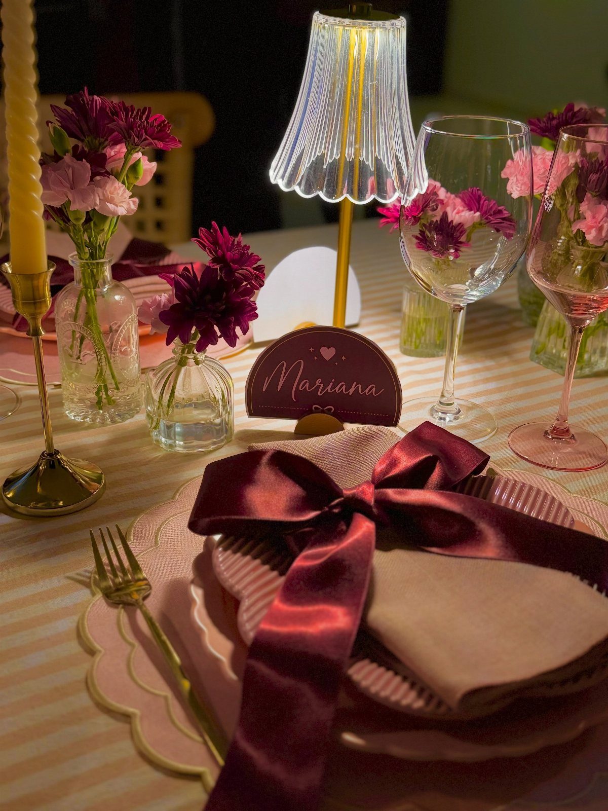 Elegant table setting with burgundy ribbons, pink plates, and small floral arrangements.