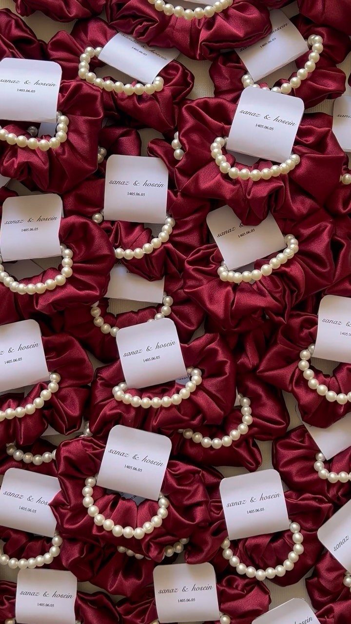 Burgundy satin scrunchies with pearl beads and white tags as wedding favors.