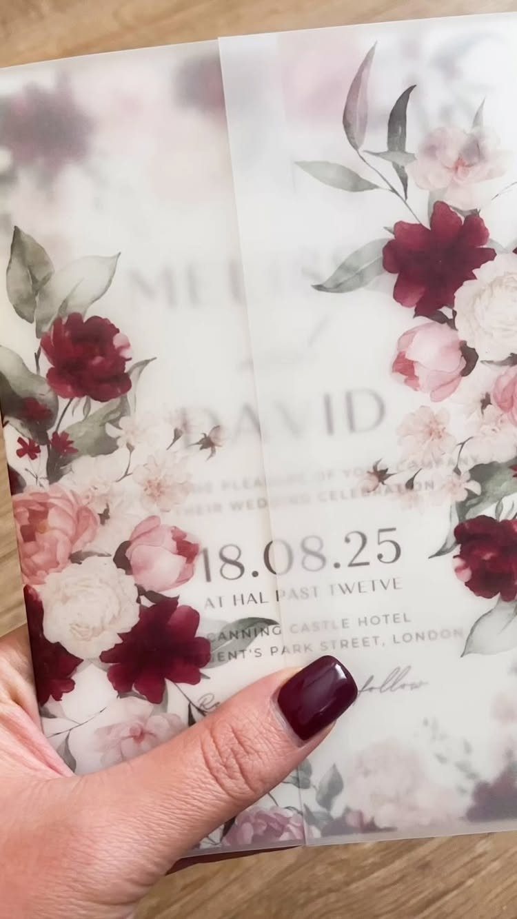 Wedding invitation with burgundy and pink flowers held by a hand with dark nails.