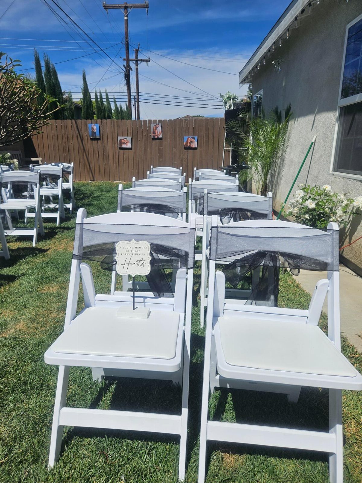 White folding chairs with grey fabric bows arranged on a green lawn for a ceremony.