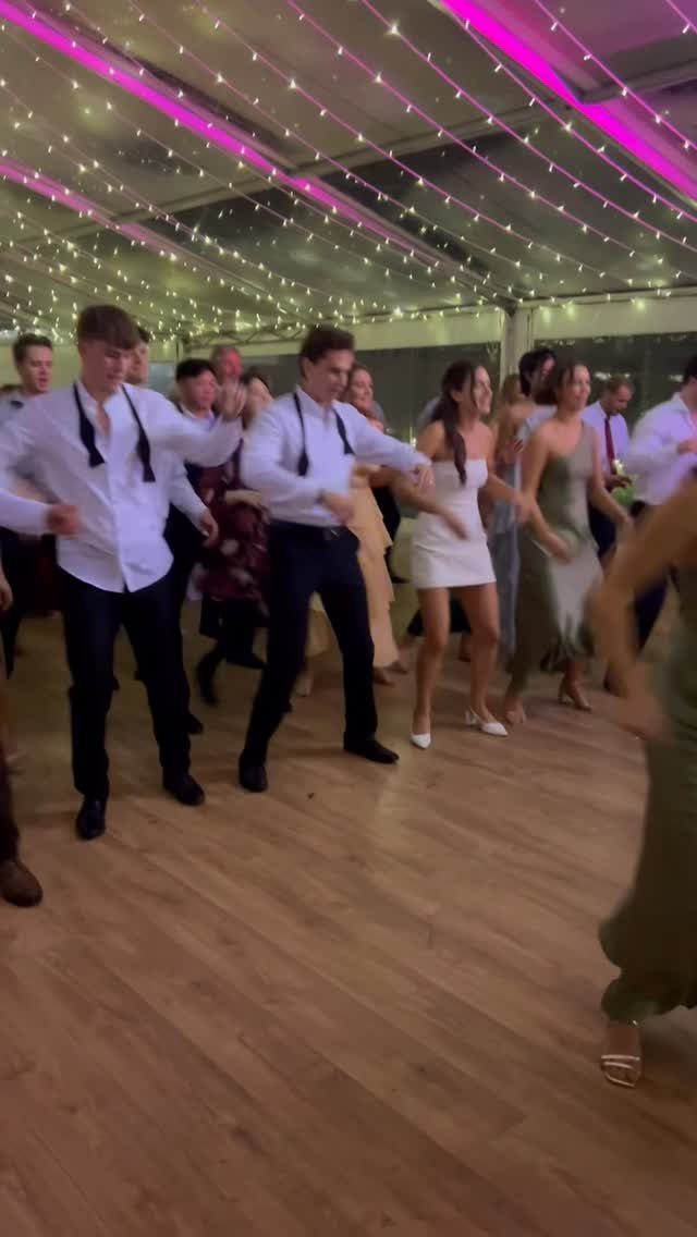Guests dancing on a wooden floor under fairy lights and pink neon strips.