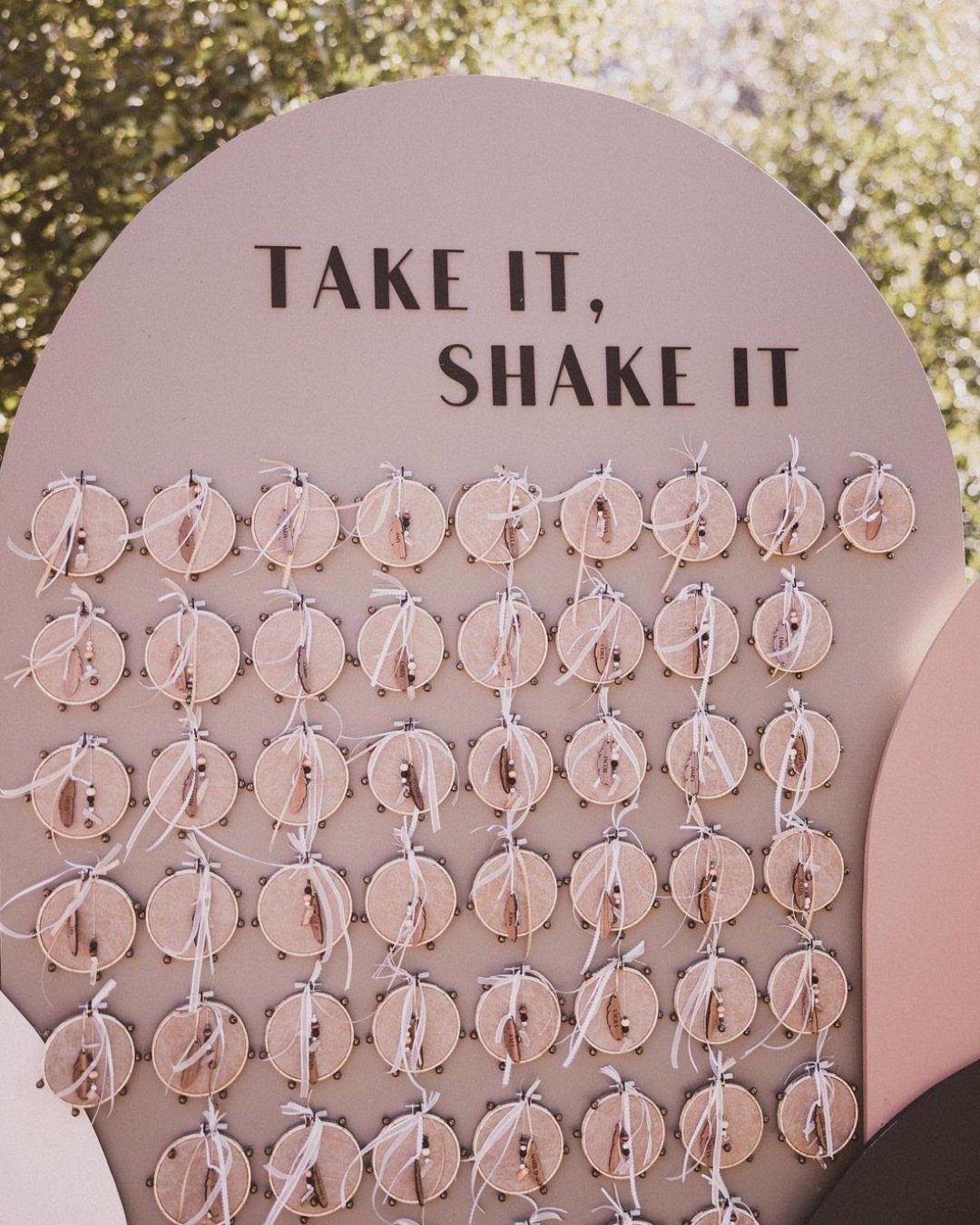Pink arched board with tambourines attached and text saying Take It, Shake It.