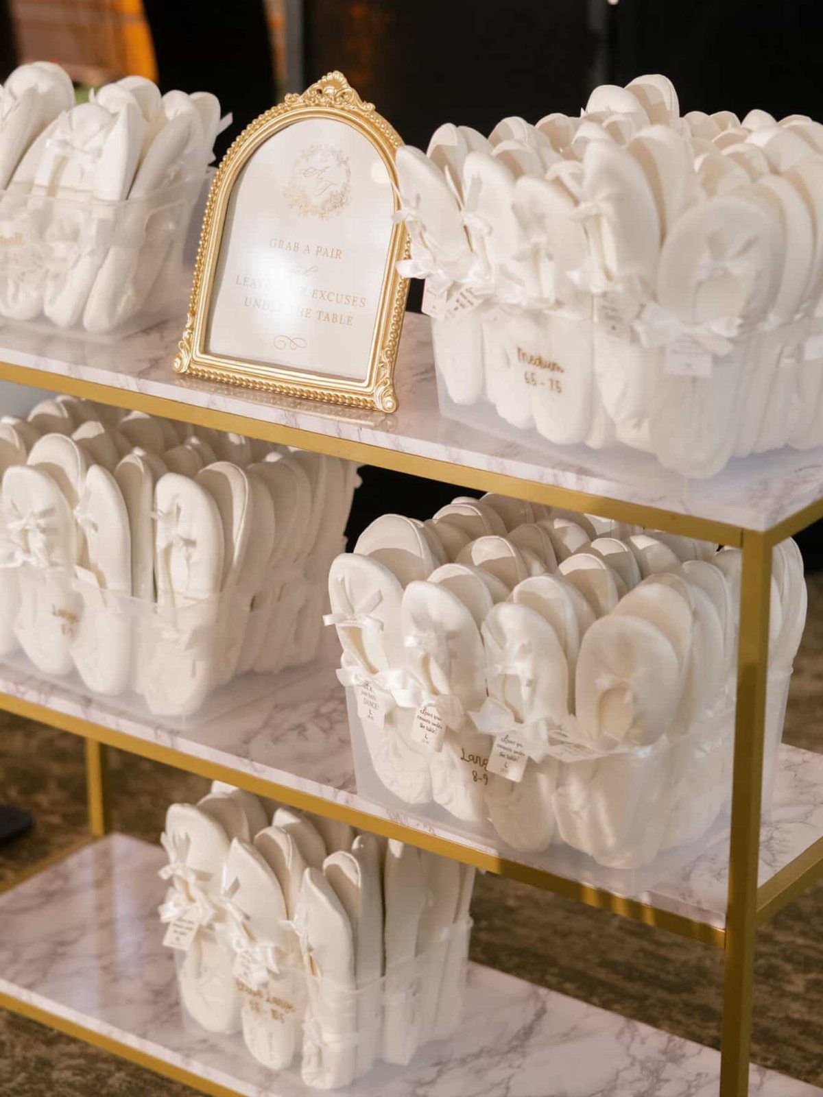 White flip-flops in baskets on a gold and marble shelf for wedding guests.