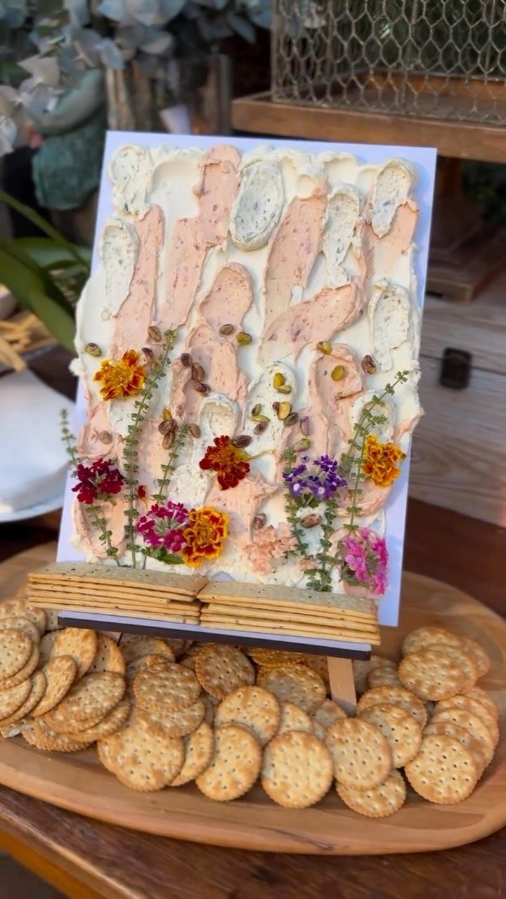 Creamy pink and white dip with edible flowers and crackers on a wooden platter.