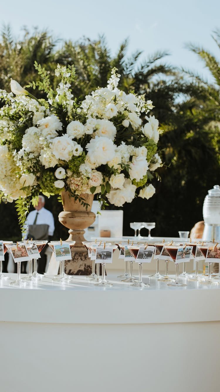 White floral centerpiece and appetizer glasses with photo cards on a white table.