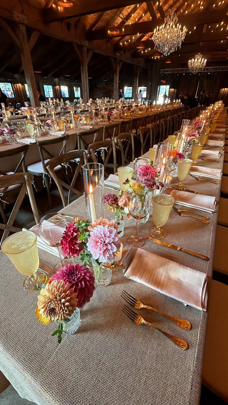 Long decorated dining table with floral centerpieces and gold cutlery in a rustic barn.