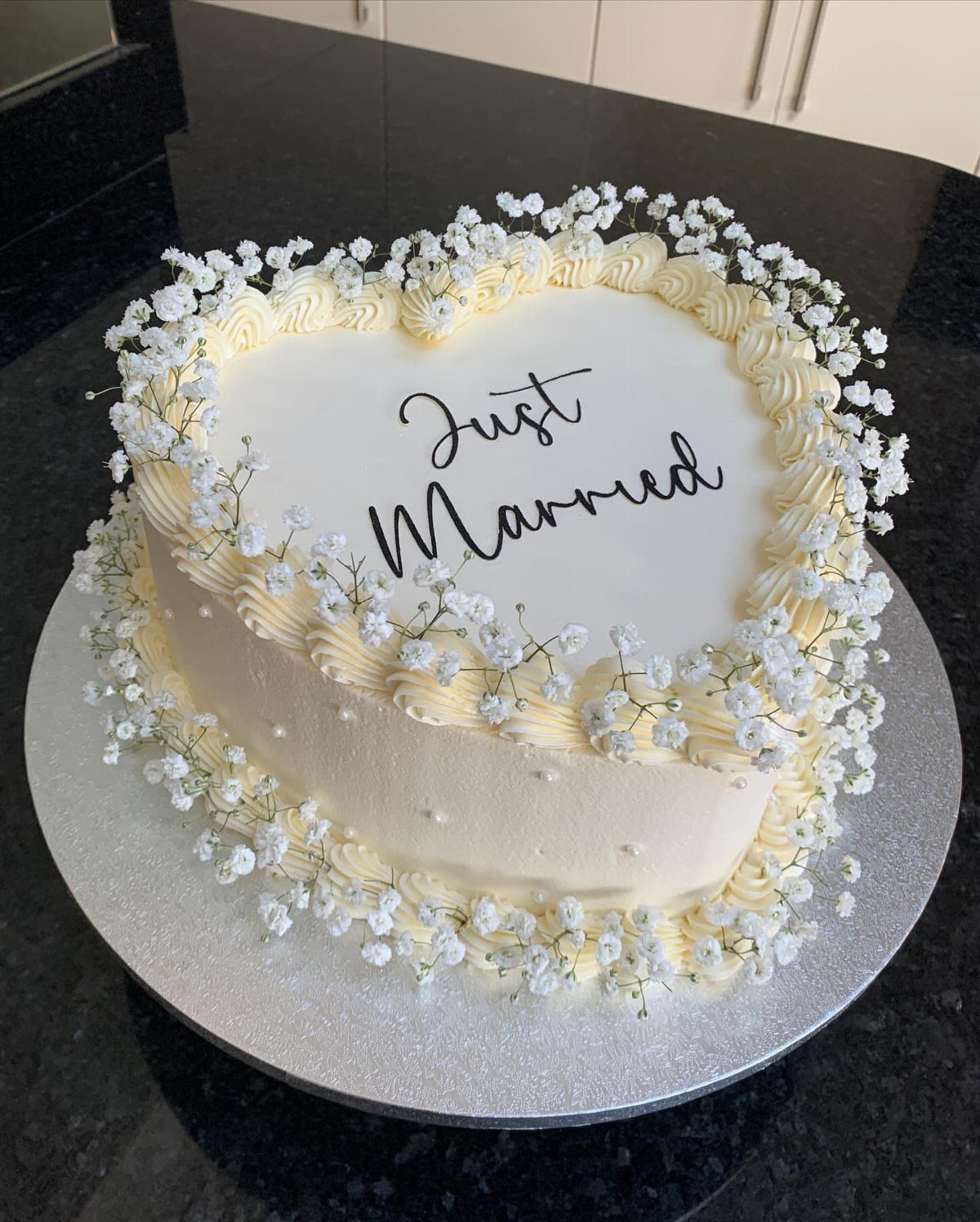 Heart-shaped white wedding cake with baby's breath flowers and Just Married text.