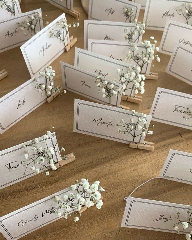 White place cards with cursive names and baby's breath flowers on a wooden table.