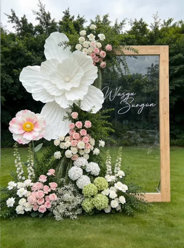 Wooden welcome sign with acrylic pane and large white paper flowers on grass