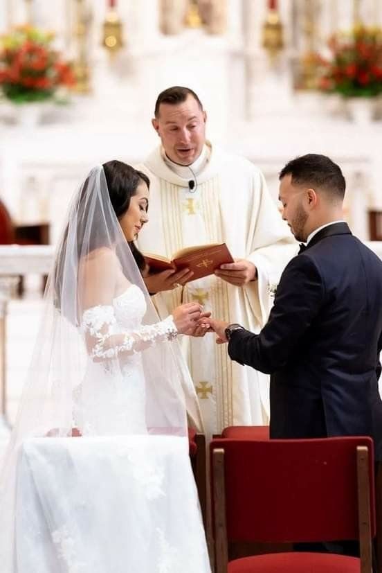 Bride and groom exchanging rings during a wedding ceremony led by a priest.