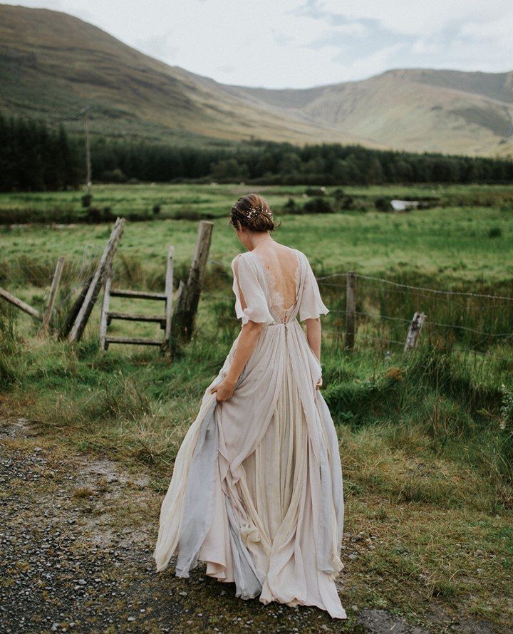 Woman in a flowing cream bohemian wedding dress standing in a mountain landscape