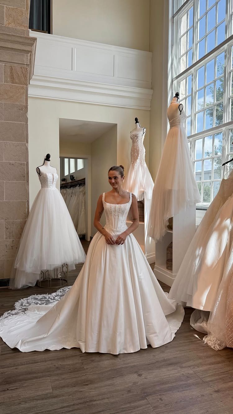 Corset Style Wedding Dress Ideas: 8 Designs to Love 3 Woman in a white corset wedding gown standing in a bright bridal boutique