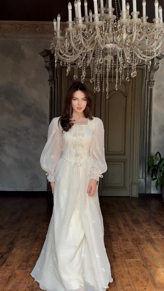 Corset Style Wedding Dress Ideas: 8 Designs to Love 4 Woman in a sheer white wedding dress with visible corset boning under a chandelier.