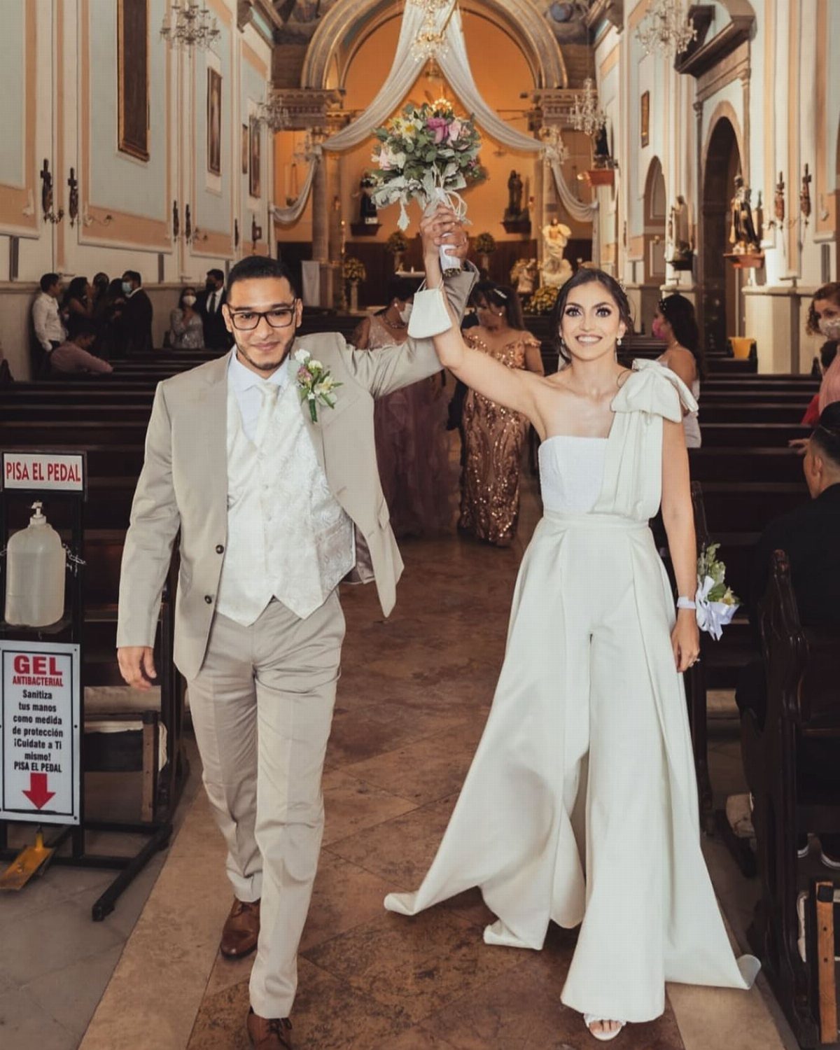9 Court Wedding Outfit Ideas, From Jumpsuits to Mini Dresses 1 Bride in white bridal jumpsuit and groom in beige suit walking in church