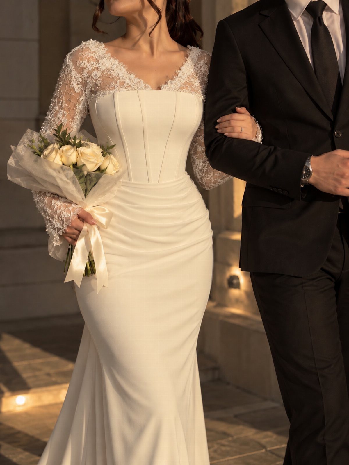 9 Court Wedding Outfit Ideas, From Jumpsuits to Mini Dresses 3 Woman in a white long sleeve wedding dress holding white roses next to groom.