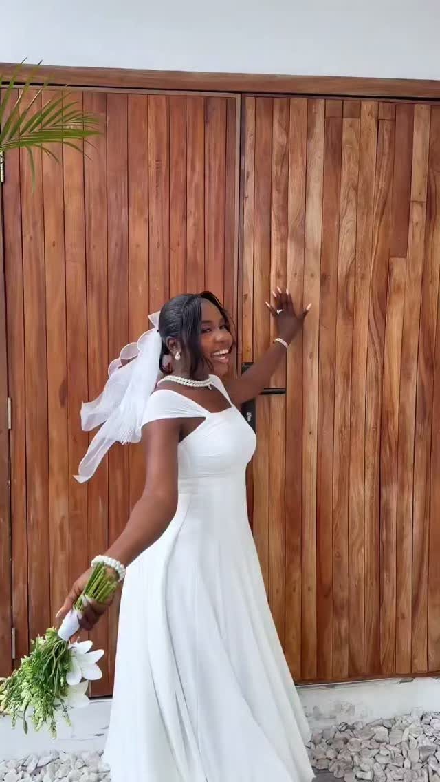 9 Court Wedding Outfit Ideas, From Jumpsuits to Mini Dresses 6 Woman in a minimalist white off-the-shoulder wedding dress holding a white floral bouquet.