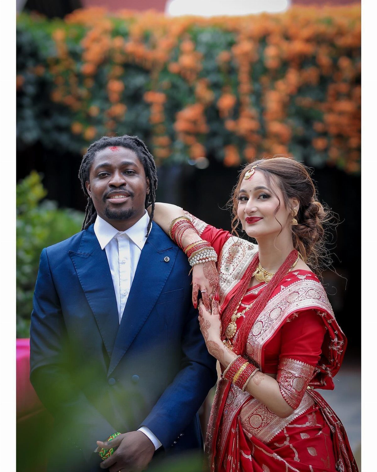 Couple in wedding attire posing together with a background of orange flowers.