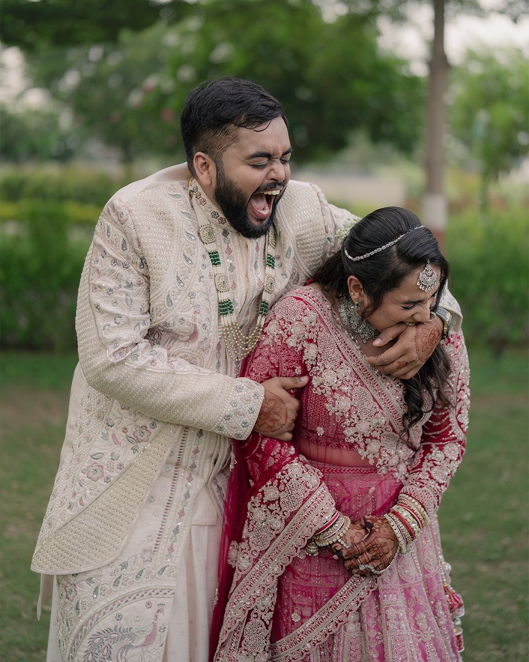 Laughing couple in traditional Indian wedding attire sharing a joyful moment outdoors