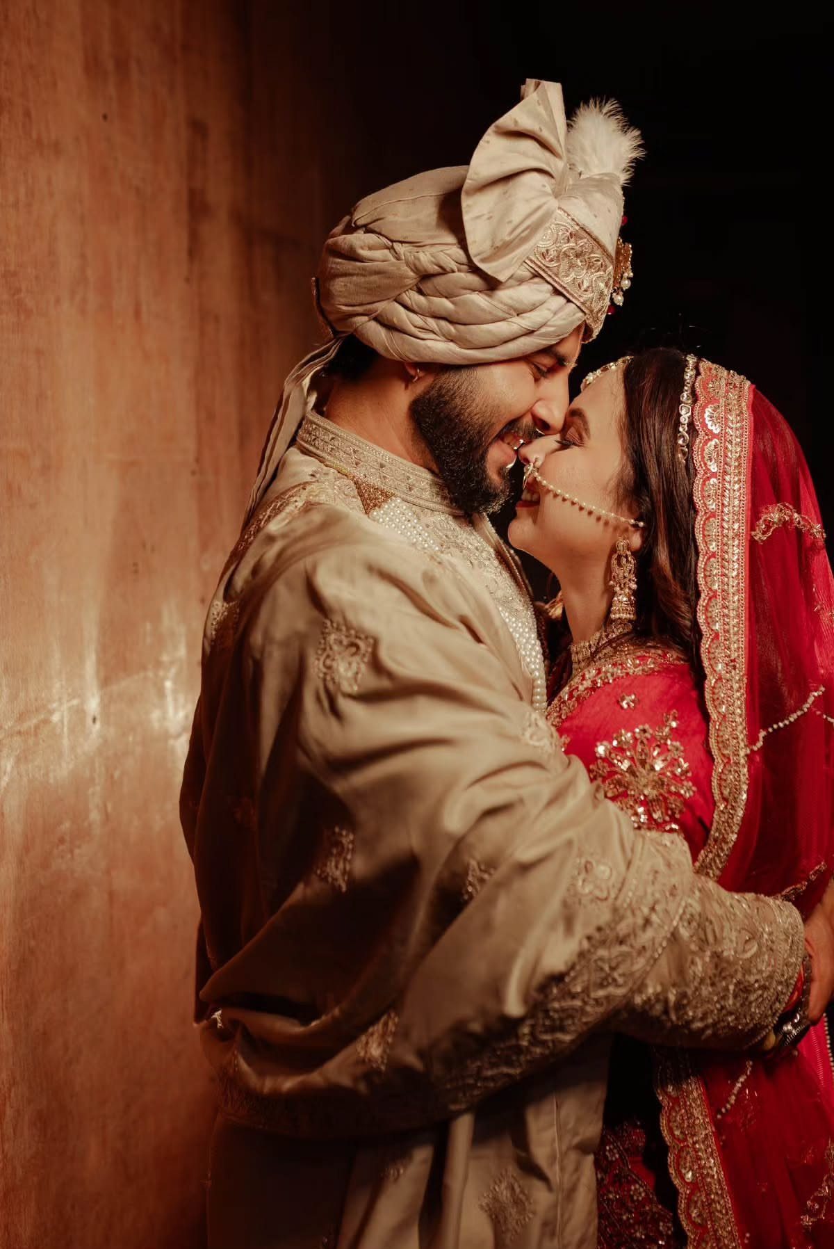 Bride and groom in traditional Indian wedding attire facing each other and smiling.