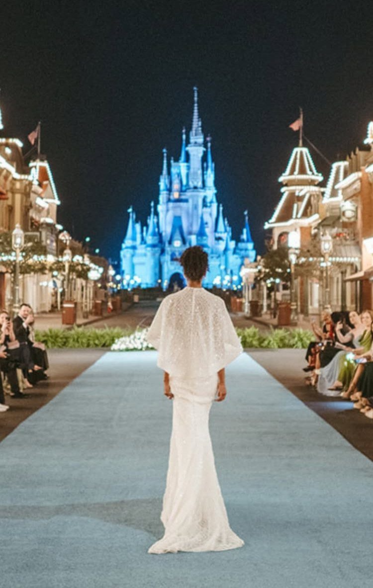 Woman in a white wedding gown standing before the illuminated Disney castle at night.