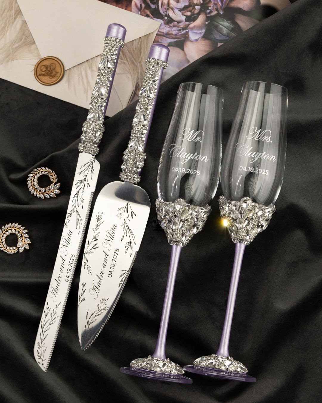 Personalized rhinestone wedding cake server, knife, and champagne flutes on black fabric.