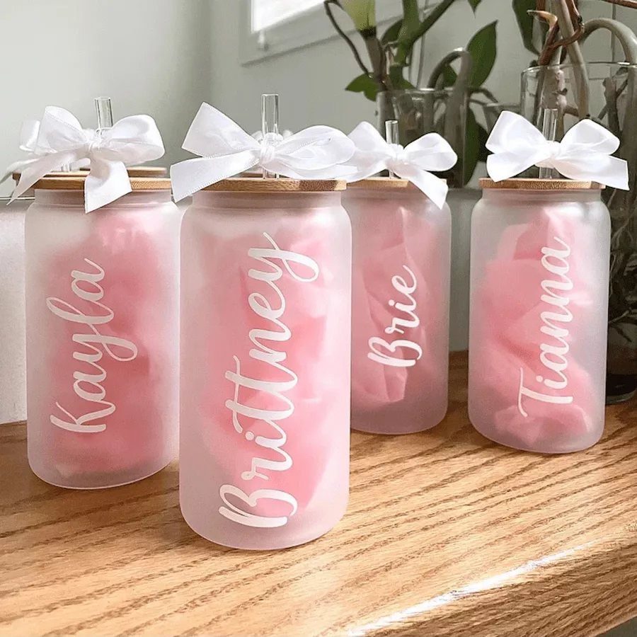 Frosted glass tumblers with bamboo lids, white bows, and personalized names in cursive script.