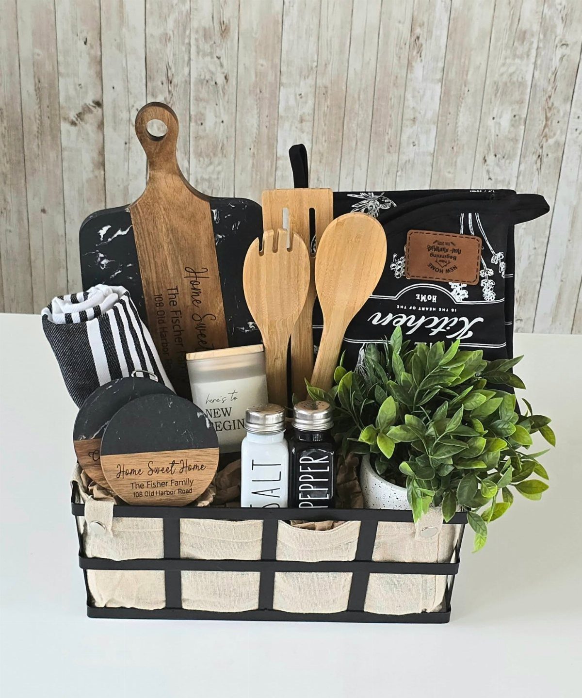 Housewarming gift basket with wooden cutting board, kitchen utensils, and a small potted plant.