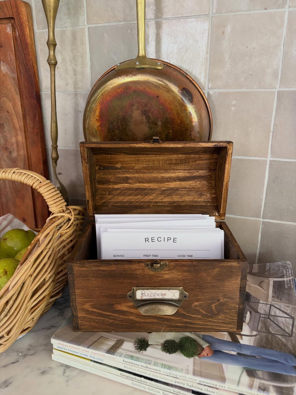 Wooden recipe box filled with white cards on a marble countertop with copper cookware.