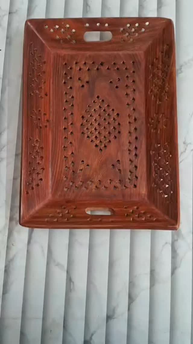 Reddish-brown wooden serving tray with decorative carvings and handle cutouts on striped background.