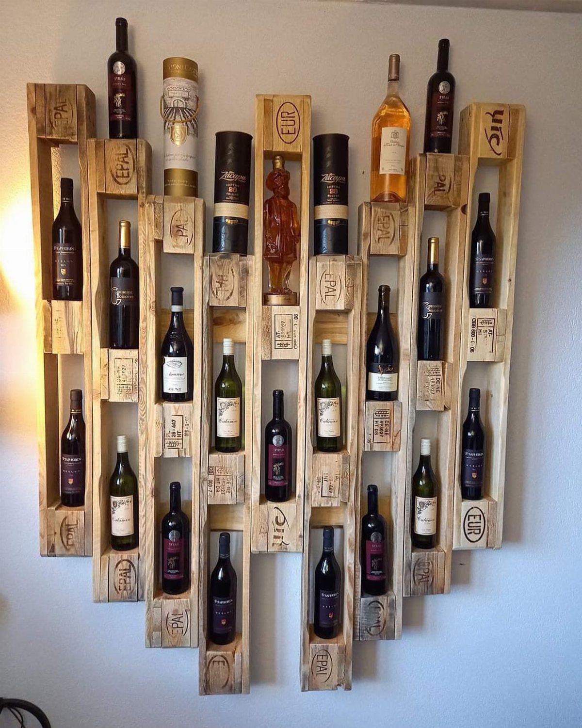 Wooden pallet wine rack mounted on a white wall holding several wine bottles.