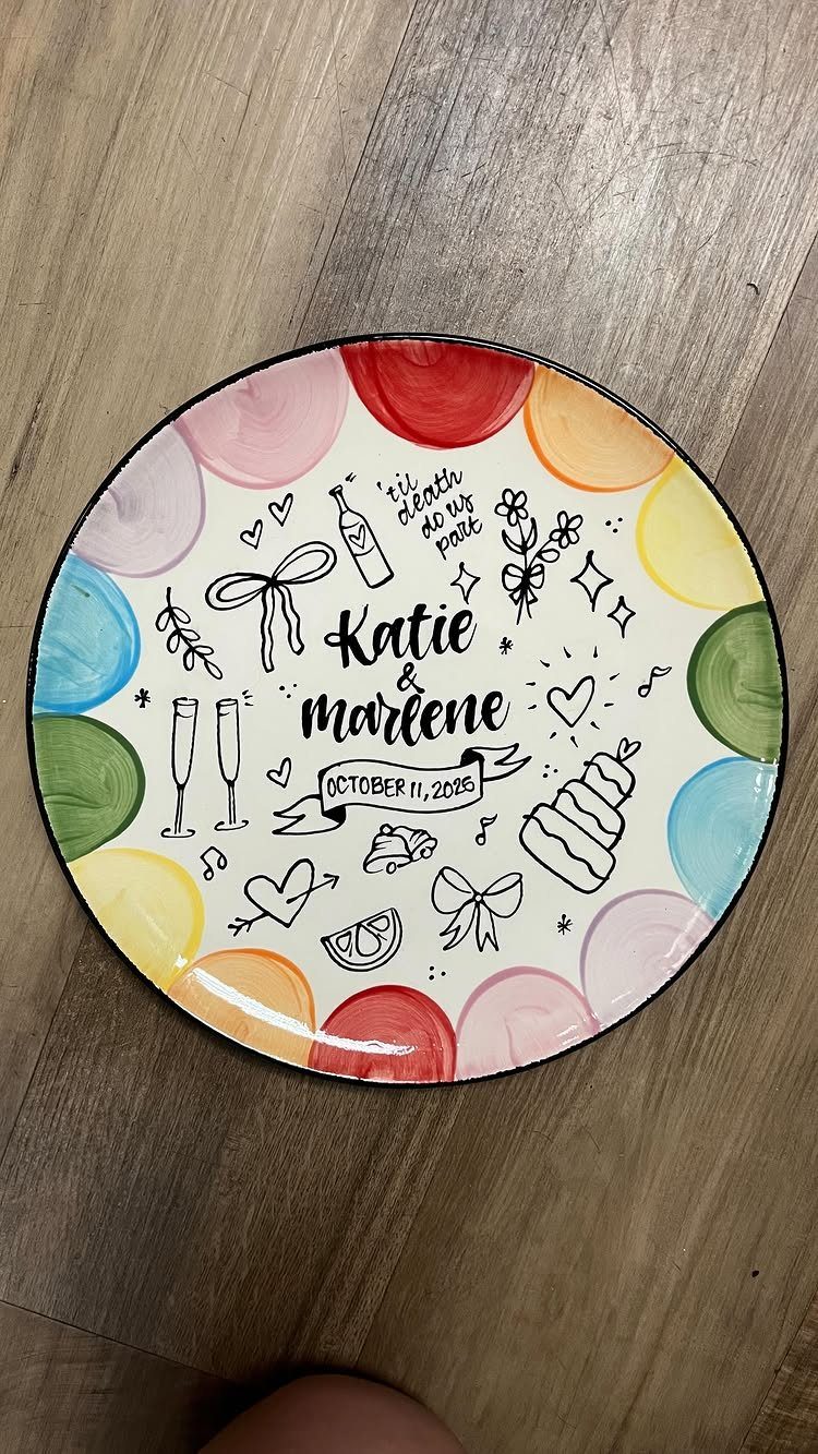 Hand-painted ceramic wedding plate with names, date, and colorful doodles on wooden background