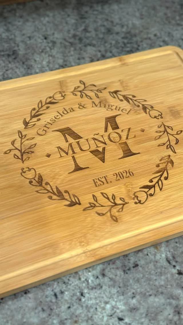Engraved wooden cutting board with names and wedding date inside a floral wreath.