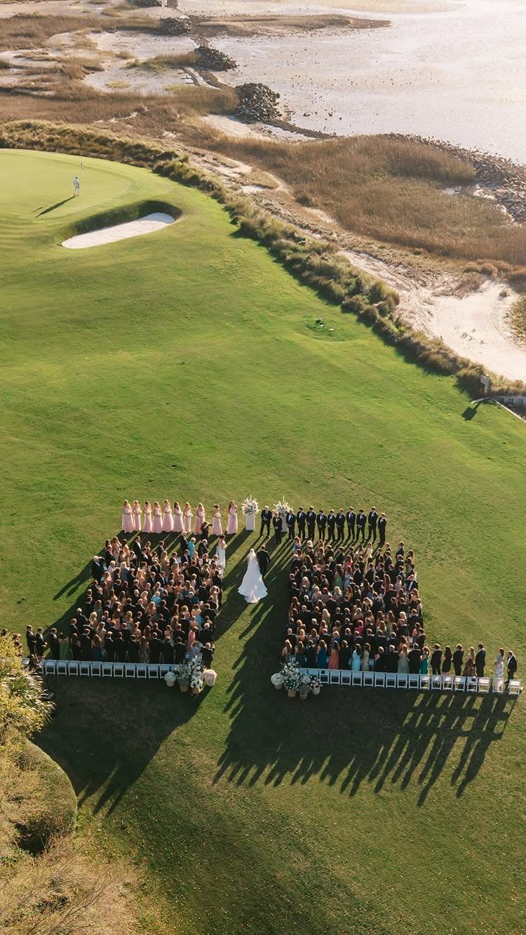Wedding ceremony on a green golf course overlooking a sandy coastline and water.
