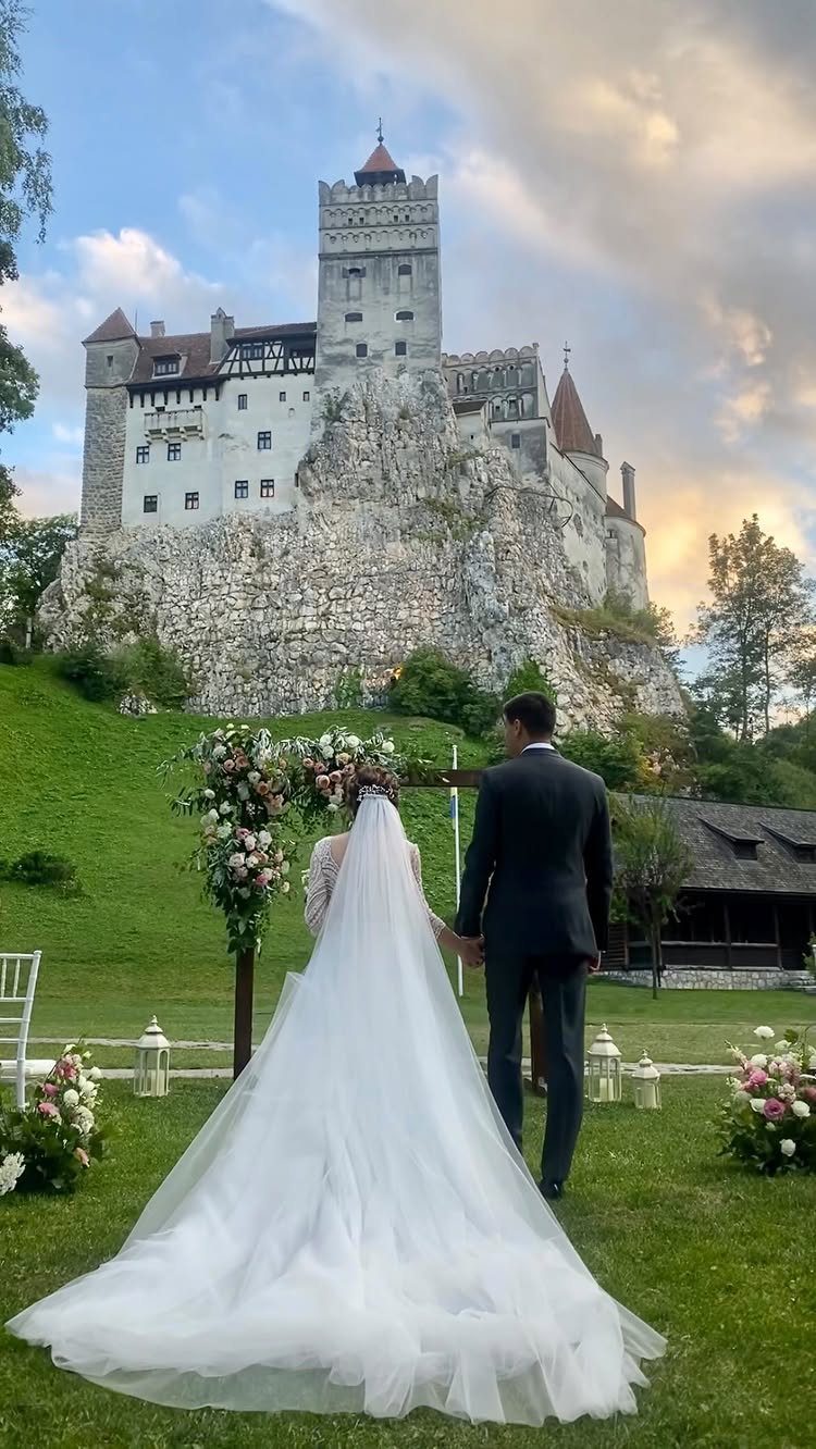 Bride and groom standing before a majestic white castle on a rocky cliff.