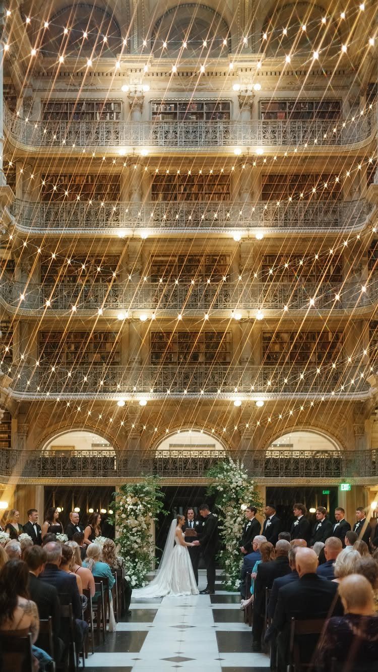 Wedding ceremony in a grand library with criss-crossing fairy lights and seated guests.