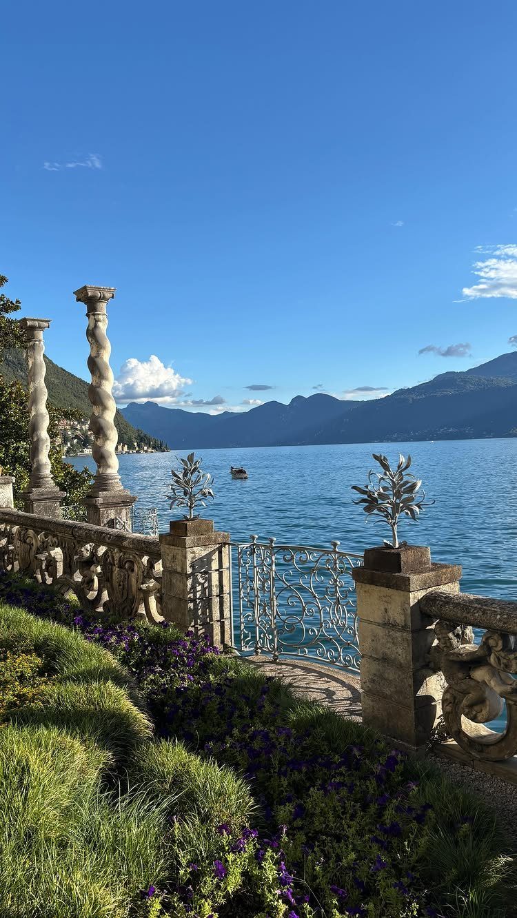 Scenic terrace with stone columns overlooking a blue lake and distant mountains.
